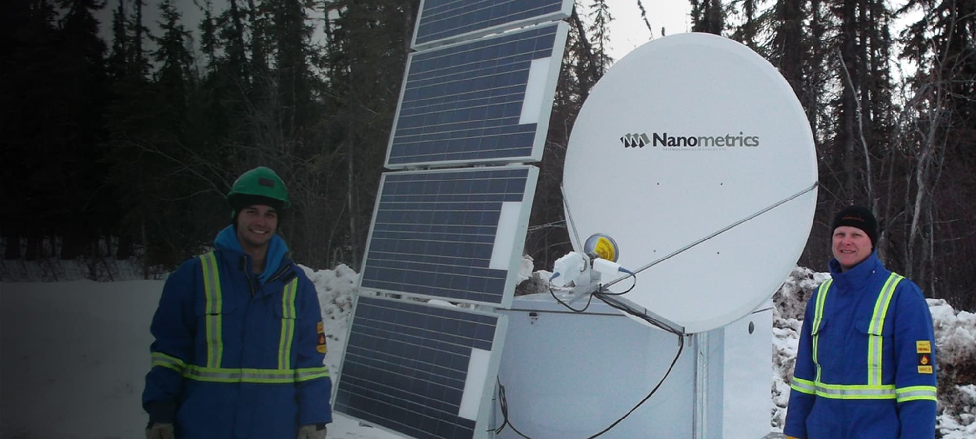 Technicians standing beside Nanometrics Seismic Array in winter conditions in wooded area