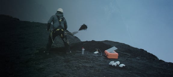 Scientist digging a hole for a seismometer near a cliff edge