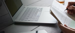 Hands writing in a notebook on top of a laptop