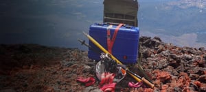 Blue deployment kit strapped to a backpack, resting near the edge of a cliff face