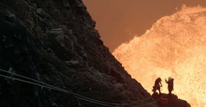 Two scientists with respirators setting up a seismometer at the top of a volcano