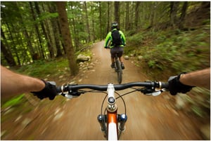 First person view of a person riding a mountain bike down a steep hill in the woods